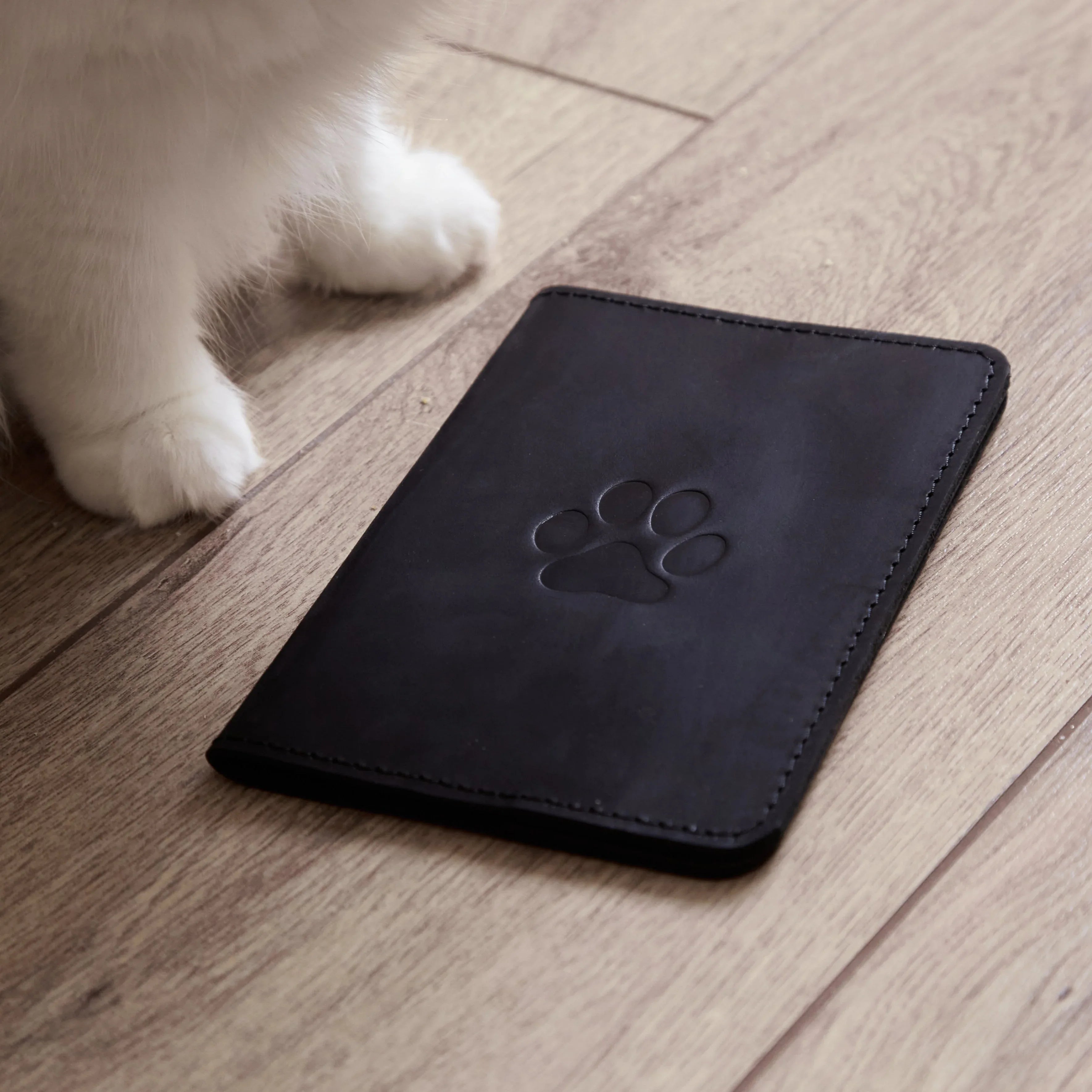 Чорна обкладинка для ветпаспорта Paw від бренду INCARNE на дерев’яній поверхні, стильний аксесуар для тварин